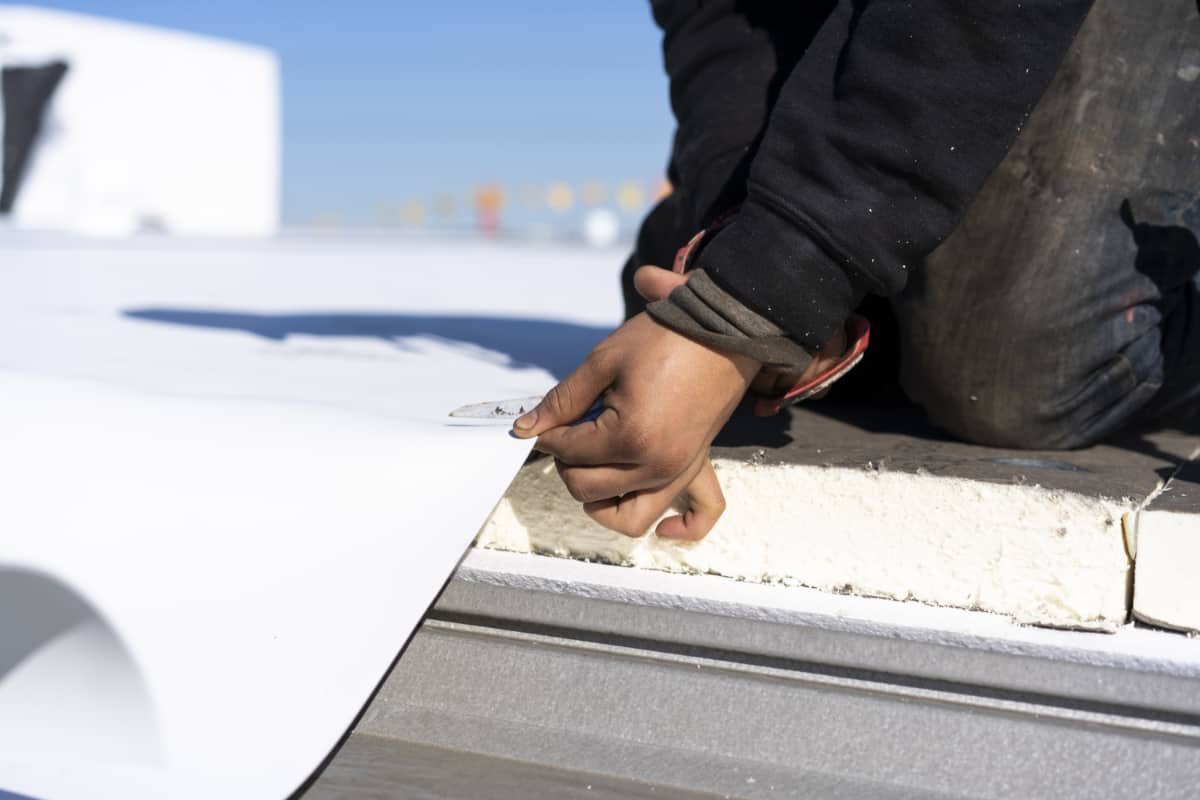 A man cutting roofing material for a roof restoration.